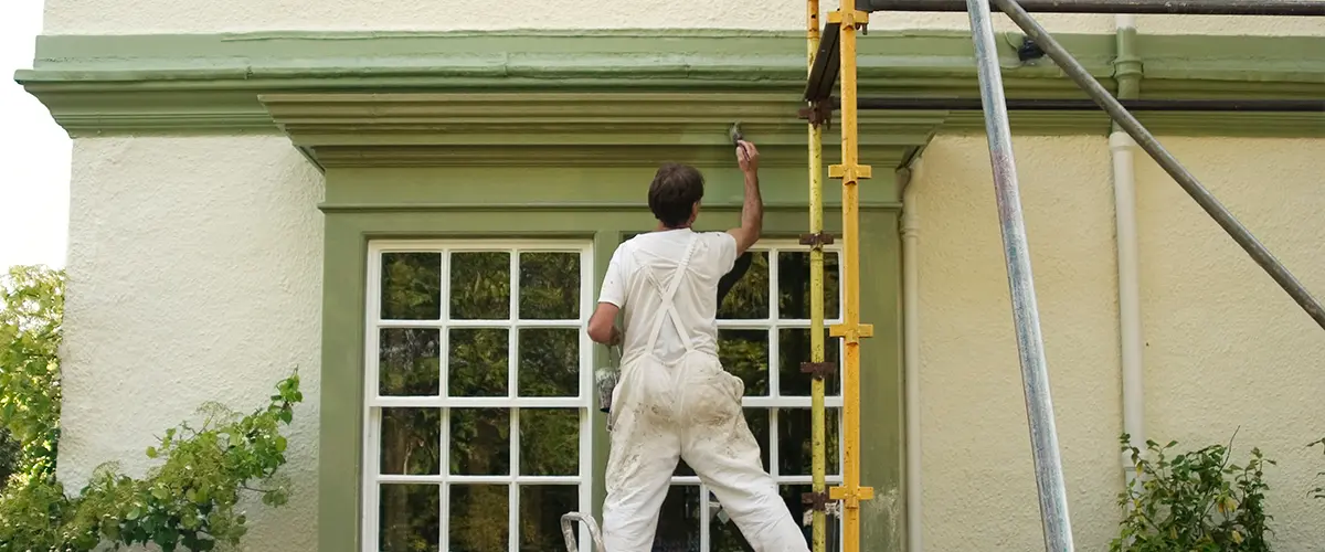 Worker painting the exterior of a building with green paint.