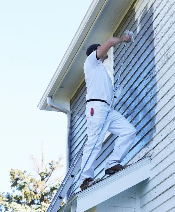contractor wearing white clothes painting a blue house in white