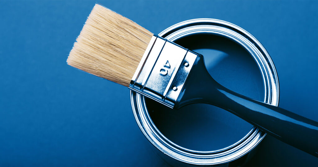 Close-up of a paintbrush resting on an open can of blue paint against a blue background