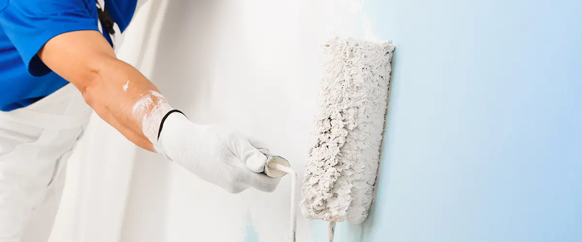 Painter using a roller to apply white paint on a blue wall