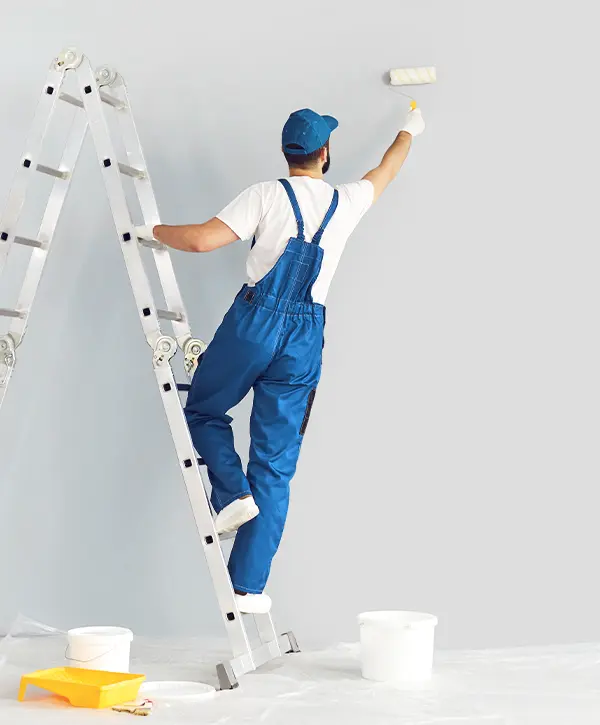 Painter on a ladder using a roller to paint a light gray wall