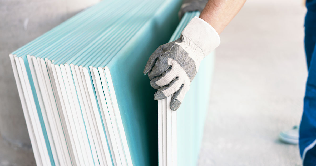 Worker handling a stack of green drywall sheets with protective gloves