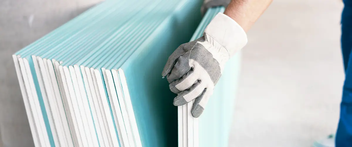 Worker handling a stack of green drywall sheets with protective gloves