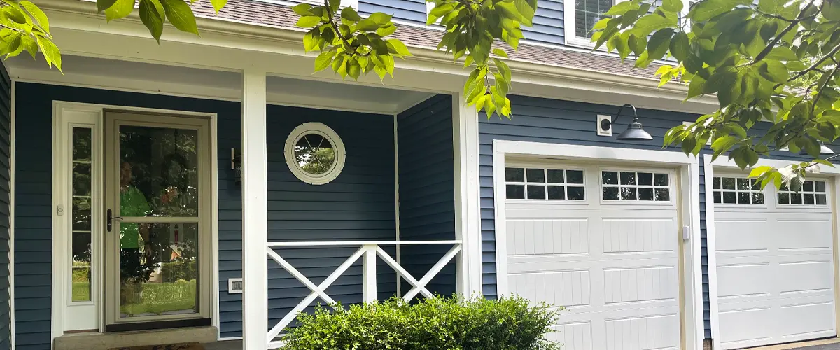 Modern front porch with blue vinyl siding, white garage doors, and stone paver entry landscaping.