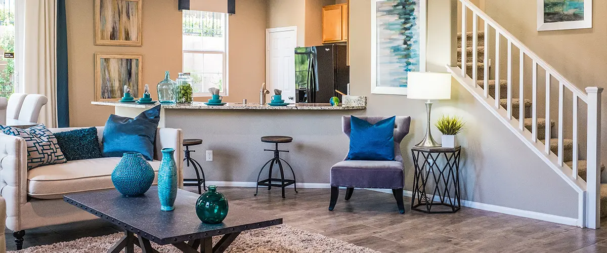 Modern living room with staircase, gray flooring, and blue accent décor in open-concept home layout