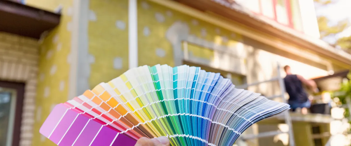 Hand holding a color fan deck in front of a house under renovation (blurred background)