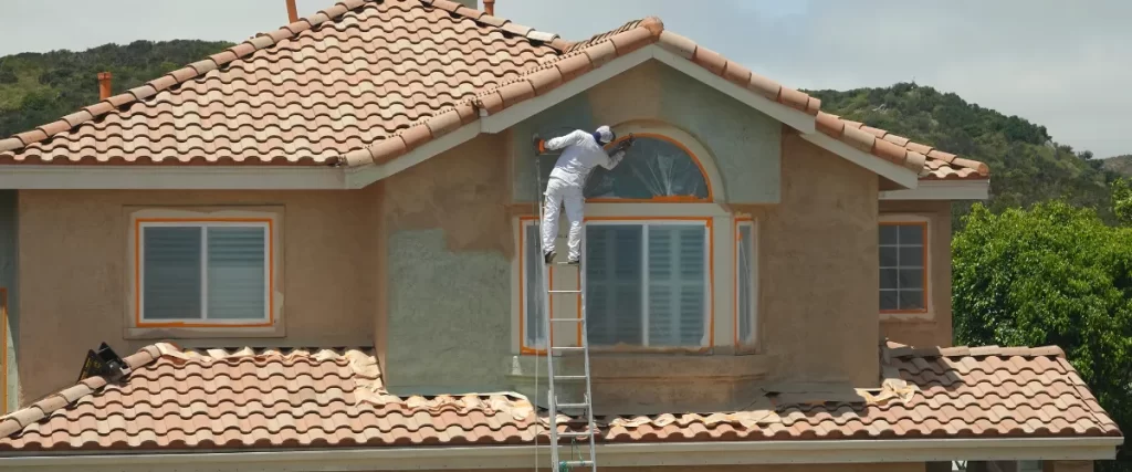 Painter on a ladder working on the stucco exterior of a Mediterranean-style home