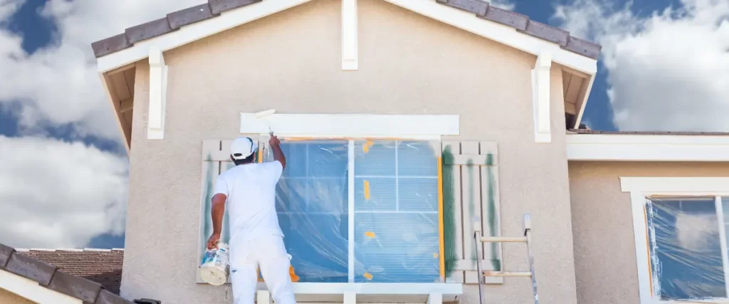 Painter covering a window with plastic sheeting before exterior painting
