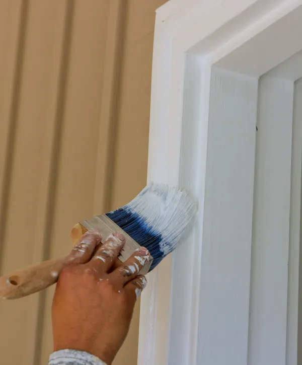 Close-up of hand painting door or window trim with white paint