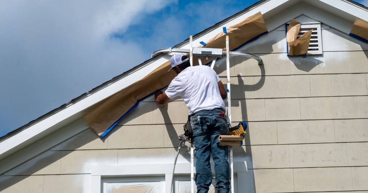 Painter on a ladder taping and prepping the exterior of a house
