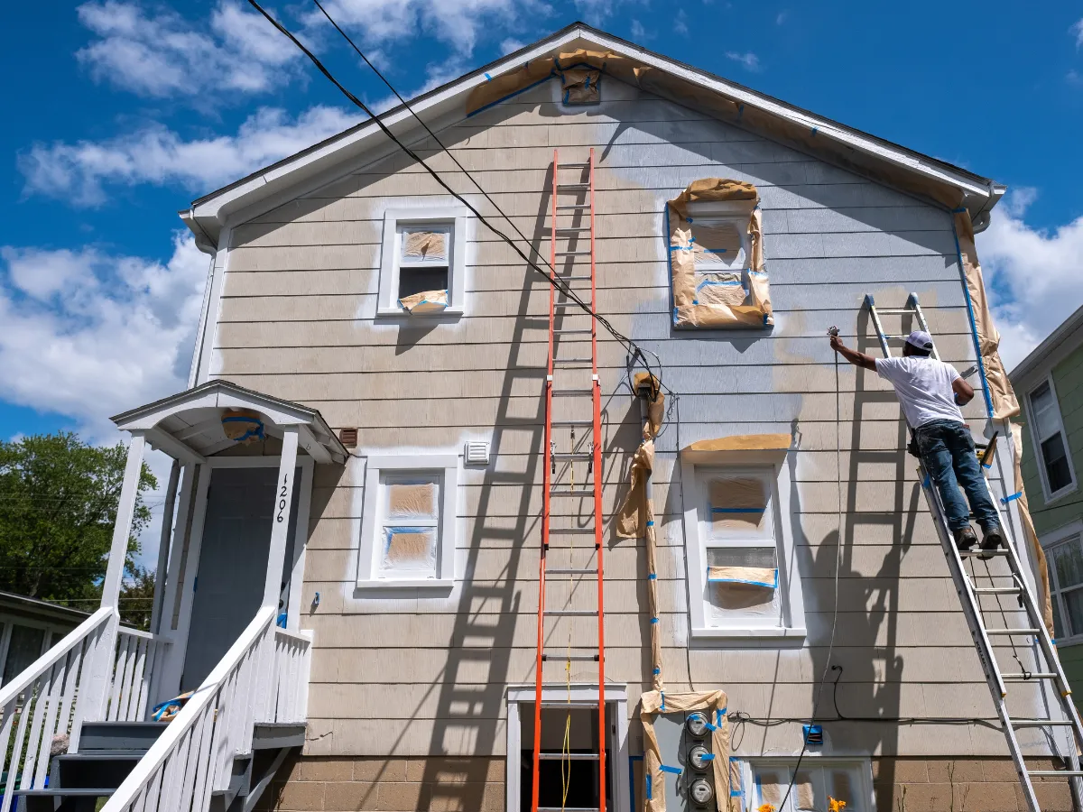House being prepped and spray painted with multiple ladders and protective coverings