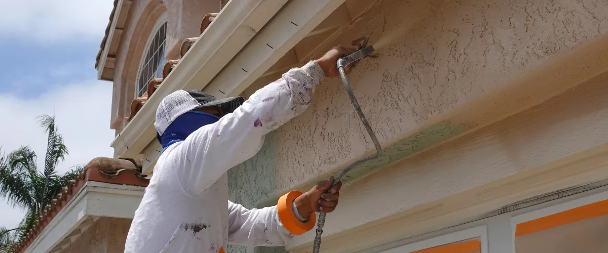 Painter spraying stucco exterior under a roofline