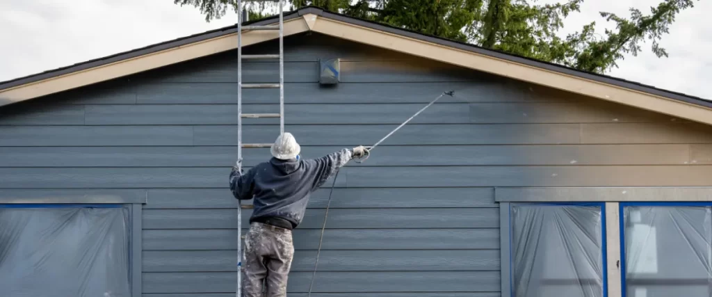 Worker using a paint sprayer to coatPainter on a ladder working on the stucco exterior of a Mediterranean-style home